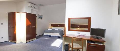 Habitación de hotel con cama, escritorio con computadora, silla, armario y espejo.