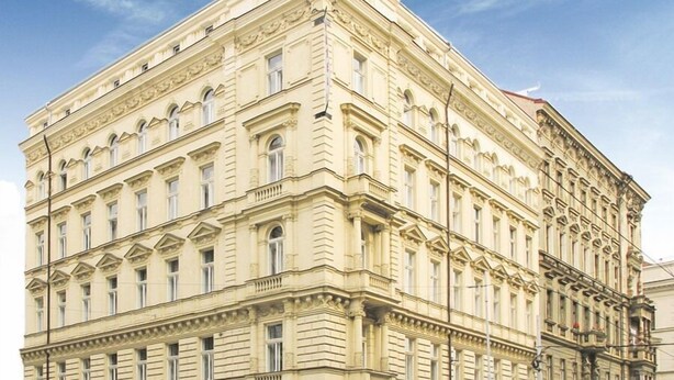 Un edificio de varios pisos con arquitectura clásica, que presenta una entrada en esquina y un café en la planta baja.