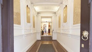 Un amplio pasillo con columnas blancas ornamentadas, suelo de mármol y una puerta con llamador de latón.