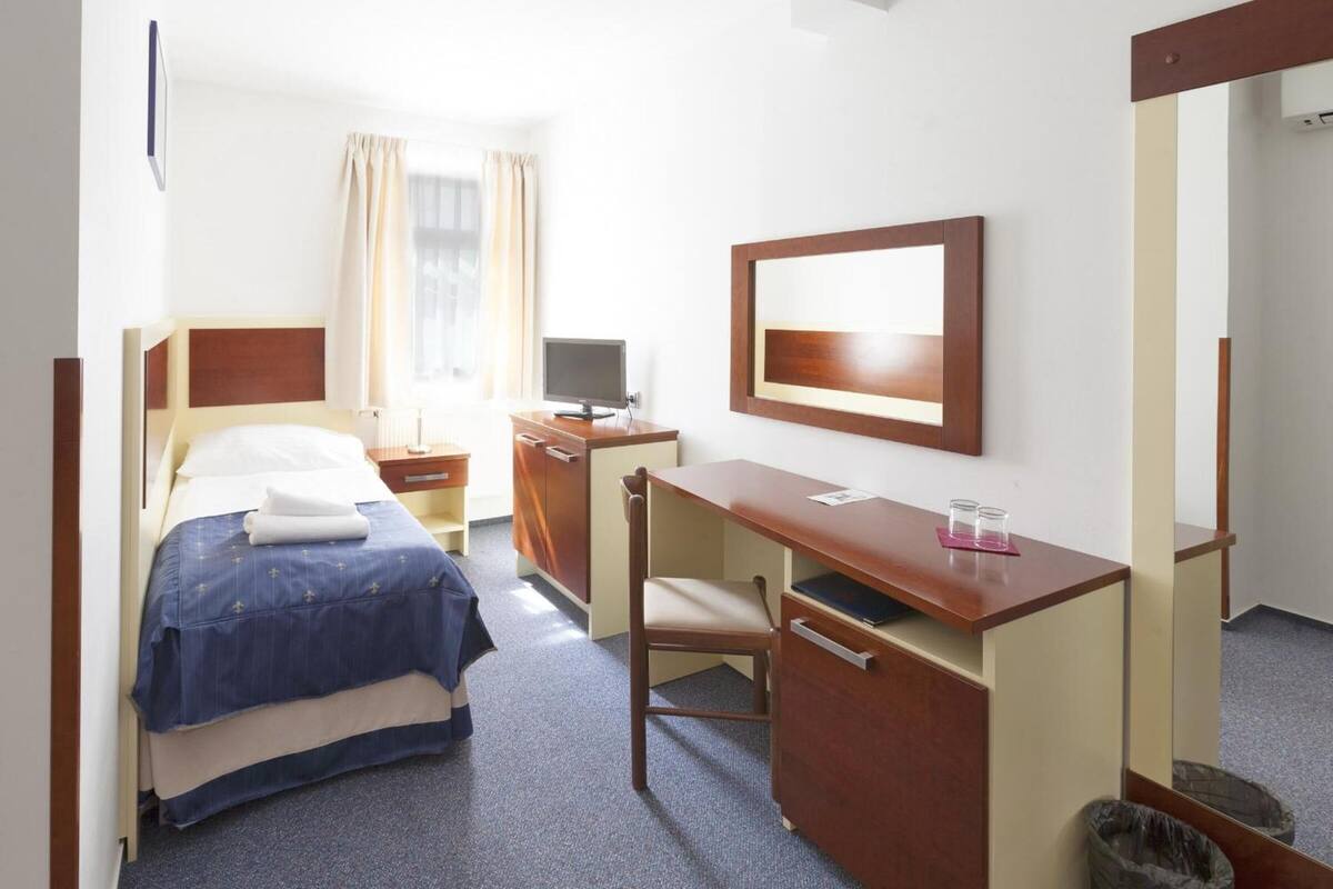 Una habitación de hotel con cama, escritorio, silla, televisor y espejo.