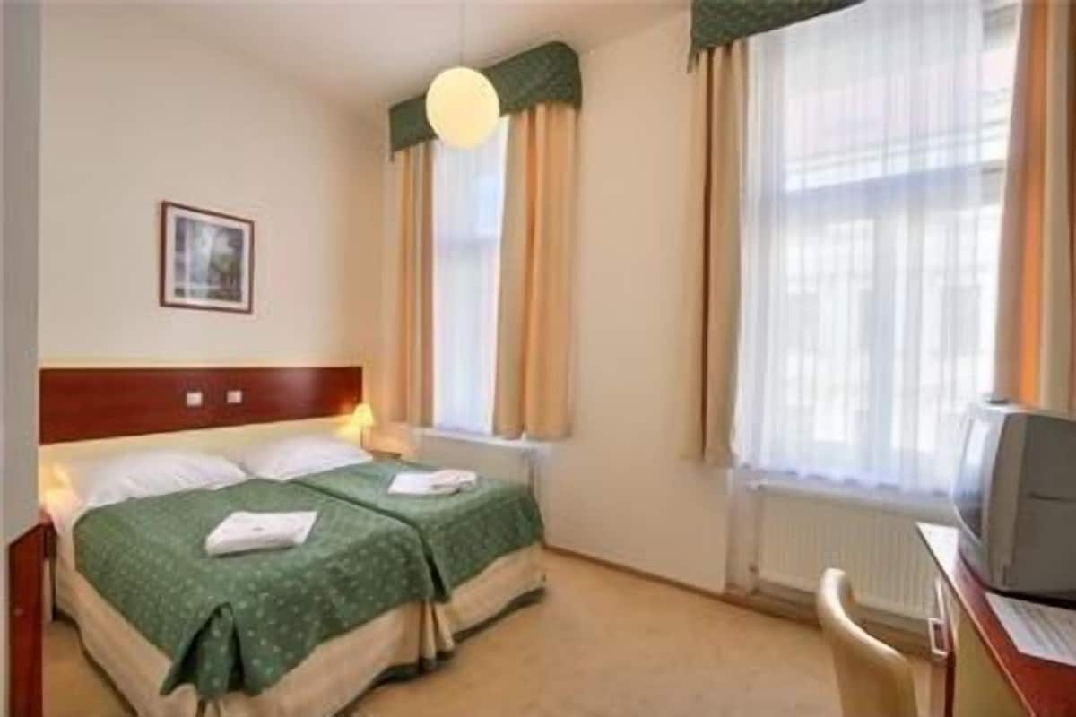 Una habitación de hotel con dos camas, un escritorio con computadora y una ventana con cortinas.
