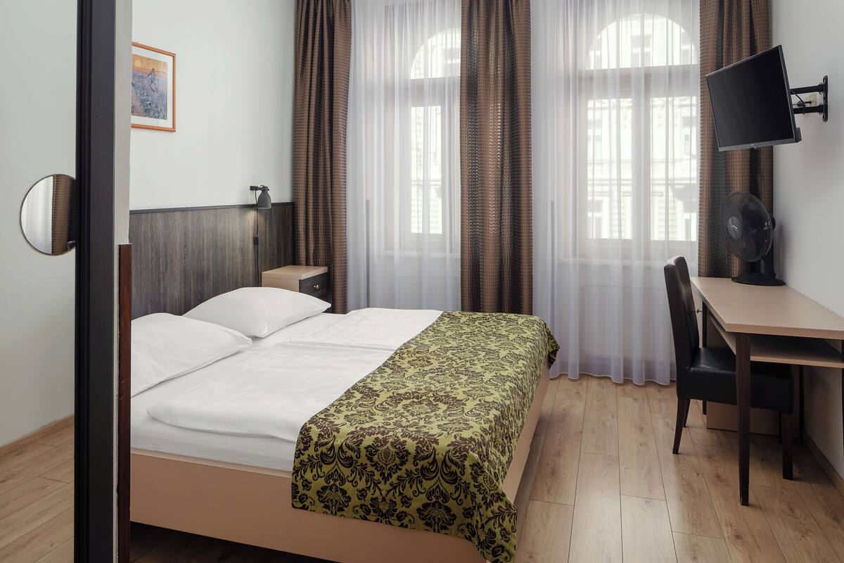 A hotel room with a bed, a desk, a chair, a TV, and a window with curtains.