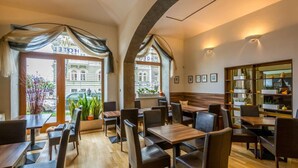 A restaurant with wooden tables and chairs, large windows with curtains, and a view of a building outside. - Hotel Superior Prague (Prague)