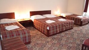 A hotel room with four beds, each with a plaid bedspread and white pillows. There are bedside lamps, a wooden bench, and a patterned carpet. - City Inn (Prague)