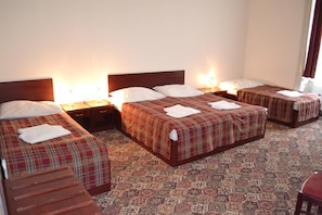 A hotel room with four beds, each with a plaid bedspread and white pillows. There are bedside lamps, a wooden bench, and a patterned carpet. - City Inn (Prague)