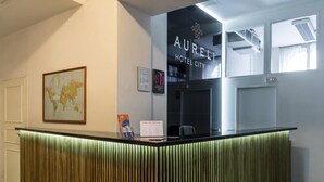 A hotel reception desk with a modern design, a world map on the wall, and a sign indicating hotel amenities. - City Inn (Prague)