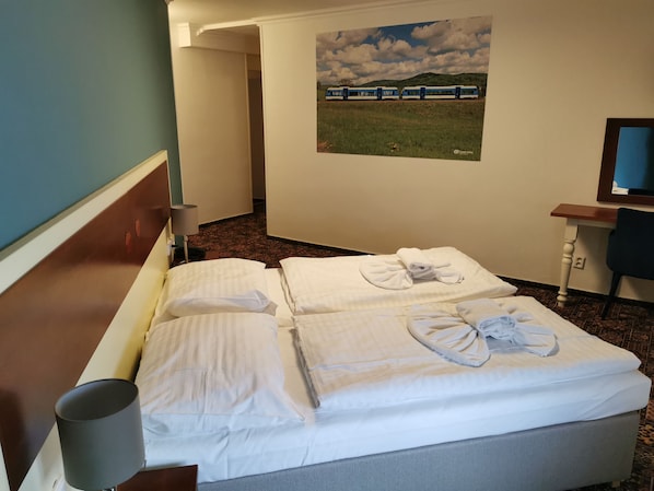 Ett hotellrum med en säng, ett skrivbord, en stol, en lampa och en tavla med ett tåg på väggen.