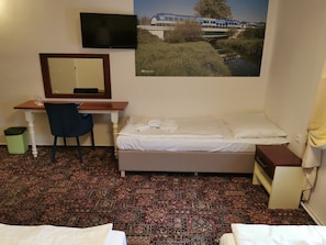 Ein kleines Hotelzimmer mit Bett, Schreibtisch, Stuhl, Fernseher und einem Bild an der Wand.