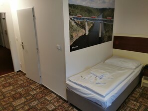 A hotel room with a bed, a patterned carpet, a door, and a poster of a bridge. - City Inn (Prague)