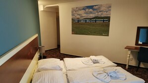 Habitación de hotel con cama, escritorio, silla, lámpara y un cuadro de un tren en la pared.
