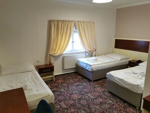 A hotel room with two single beds, a small bedside table with a lamp, a window with curtains, and a patterned carpet. - City Inn (Prague)