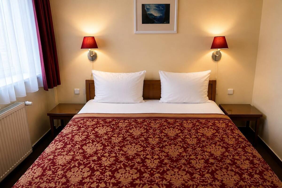A hotel room with a large bed, two bedside tables, a radiator, and two wall-mounted lamps.