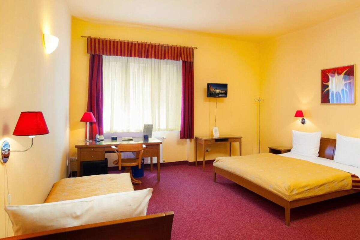A hotel room with two beds, a desk, a chair, a television, and a window with curtains.