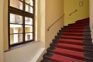 Una scala con gradini rivestiti di tappeto rosso e una ringhiera, che porta a un pianerottolo con una finestra che si affaccia su un balcone.