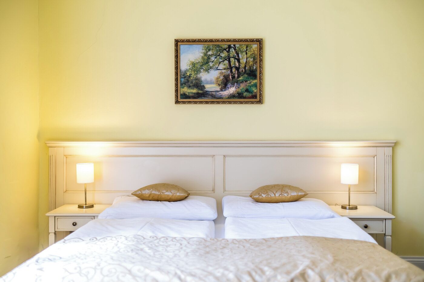 A double bed with two nightstands, each with a lamp, in a room with a painting on the wall.