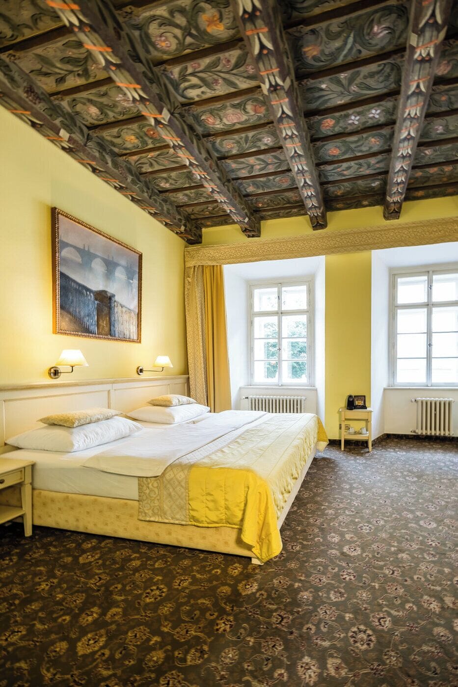 Una habitación de hotel con una cama grande, dos mesitas de noche, un cuadro y una ventana.