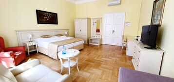 Quarto de hotel com cama, escrivaninha, cadeira, televisão e guarda-roupa.