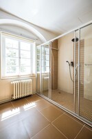 A bathroom with a glass shower enclosure, a window, and a radiator.