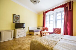 Quarto de hotel com cama, televisão, escrivaninha, cadeira e janela com cortinas.