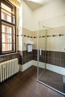 Un bagno con cabina doccia in vetro, termosifone e finestra con persiane.