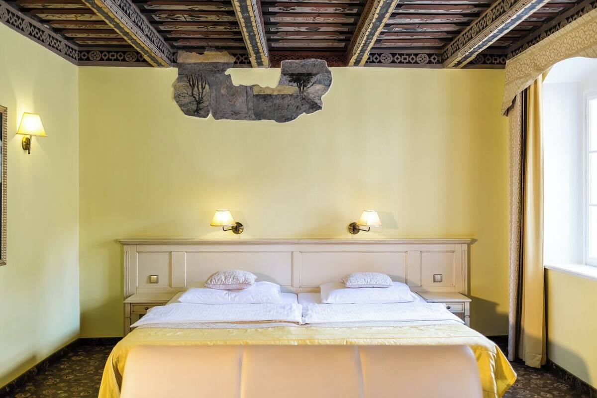 Une chambre d’hôtel comprenant un lit, deux tables de chevet, des appliques murales, un élément décoratif au plafond et une fenêtre.