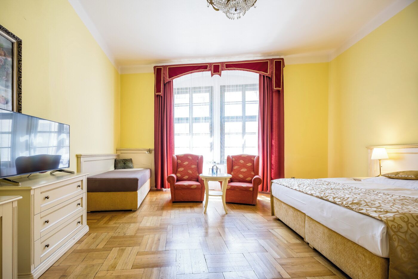 A hotel room with a bed, a TV, a desk, and two armchairs.