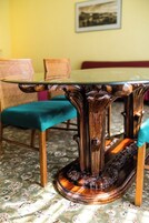 Uma mesa com pés ornamentados e tampo verde, colocada sobre um tapete estampado em um quarto com parede amarela e uma moldura com imagem.