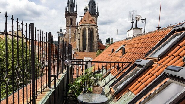 A rooftop terrace with a table and chairs, a wrought iron fence, and a view of a church with twin spires. - Hotel Metamorphis (Prague)