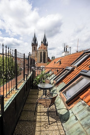 Una terraza en la azotea con una mesa y sillas, una barandilla de hierro forjado y vistas a una iglesia con dos torres.
