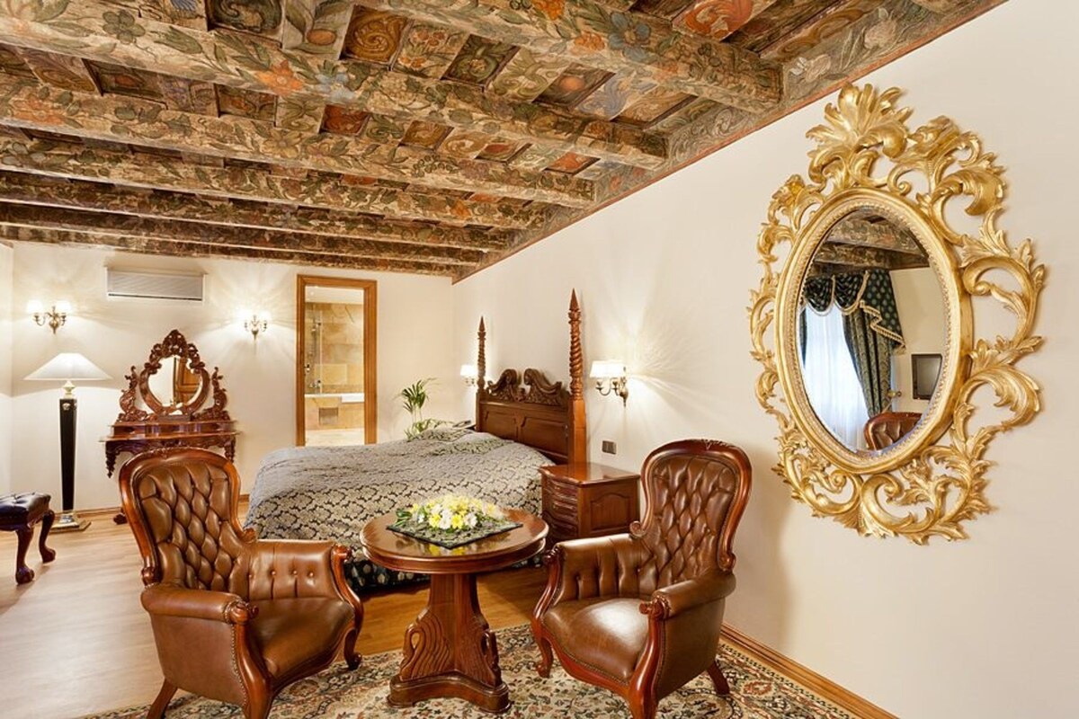 Un dormitorio lujoso con una cama grande, muebles ornamentados, un techo decorativo y un espejo con un marco elaborado.