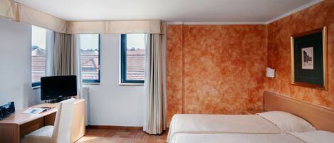 Ein Hotelzimmer mit Bett, Schreibtisch, Fernseher und einem fensterbepflanzten Fenster.