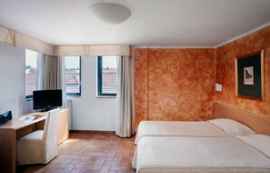 A hotel room with a bed, a desk, a television, and a window with curtains.