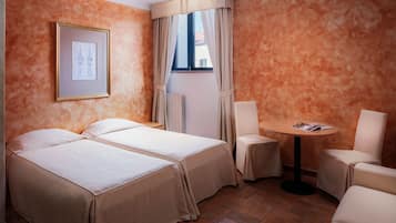 Quarto de hotel com duas camas, uma mesa redonda pequena, uma cadeira e um quadro na parede.