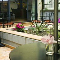 Un área de estar al aire libre con una mesa y sillas, un jarrón de flores y una jardinera con plantas y flores.