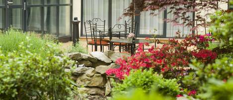 Un patio con una mesa y sillas, rodeado de un jardín con diversas plantas y flores.
