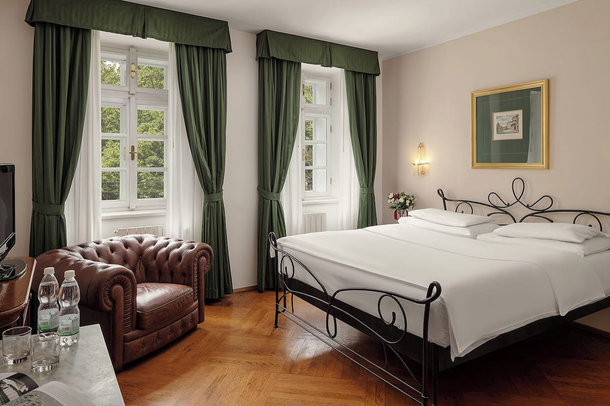 A bedroom with a bed, a leather armchair, a table with glasses and bottles, and a framed picture on the wall.