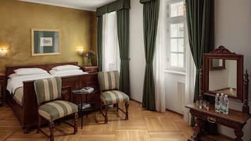 Quarto com cama de madeira, duas poltronas estofadas, uma mesinha, um espelho e um quadro pendurado na parede.