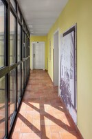 Um corredor com chão de azulejos, uma porta branca ao fundo e um cartaz na parede.
