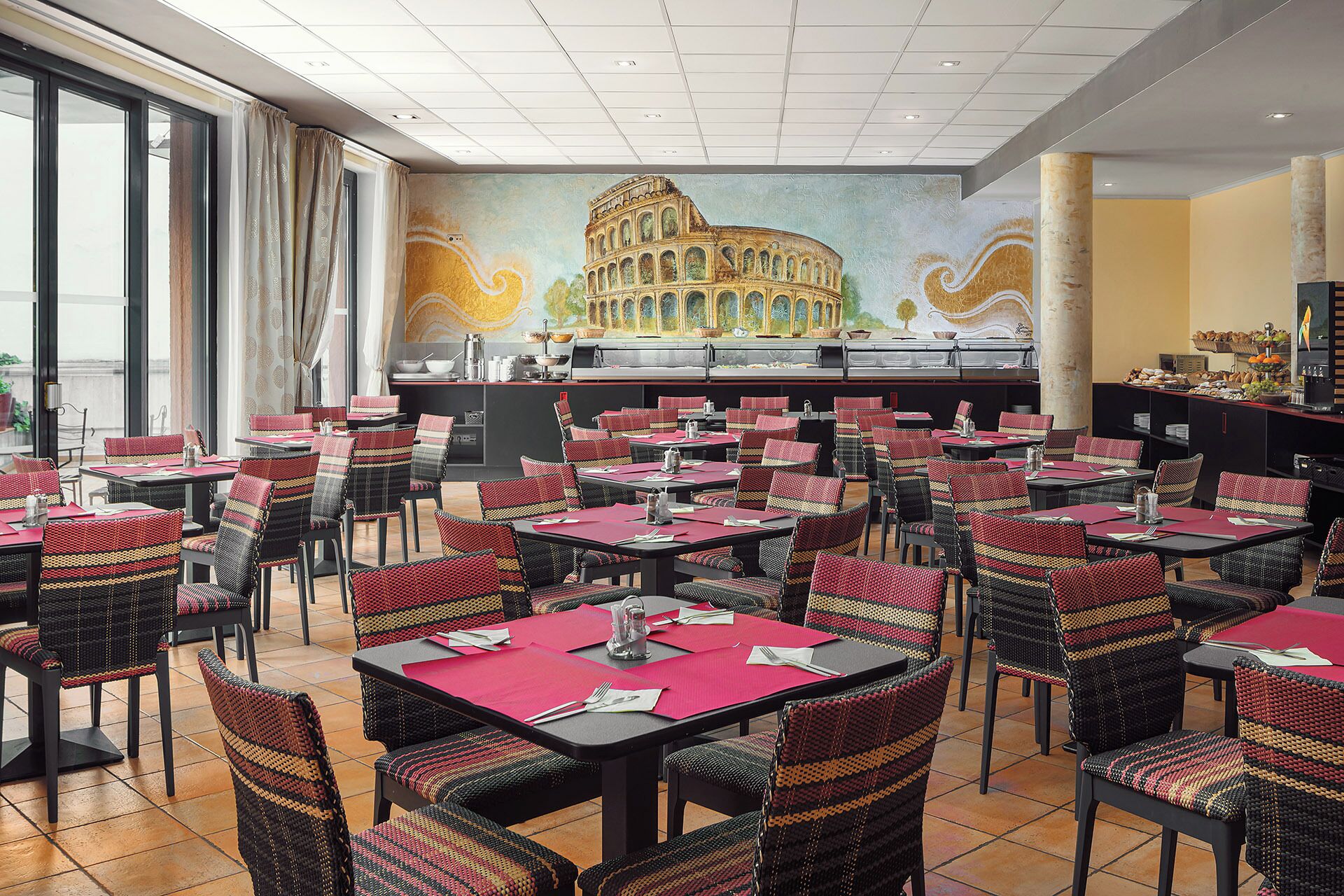 Un restaurante con varias mesas y sillas, un mural del Coliseo y una zona de buffet.
