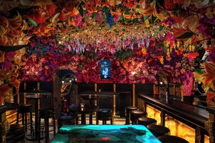 Uma área de bar com uma parede floral, vários bancos e uma mesa central com um recurso aquático iluminado em azul.