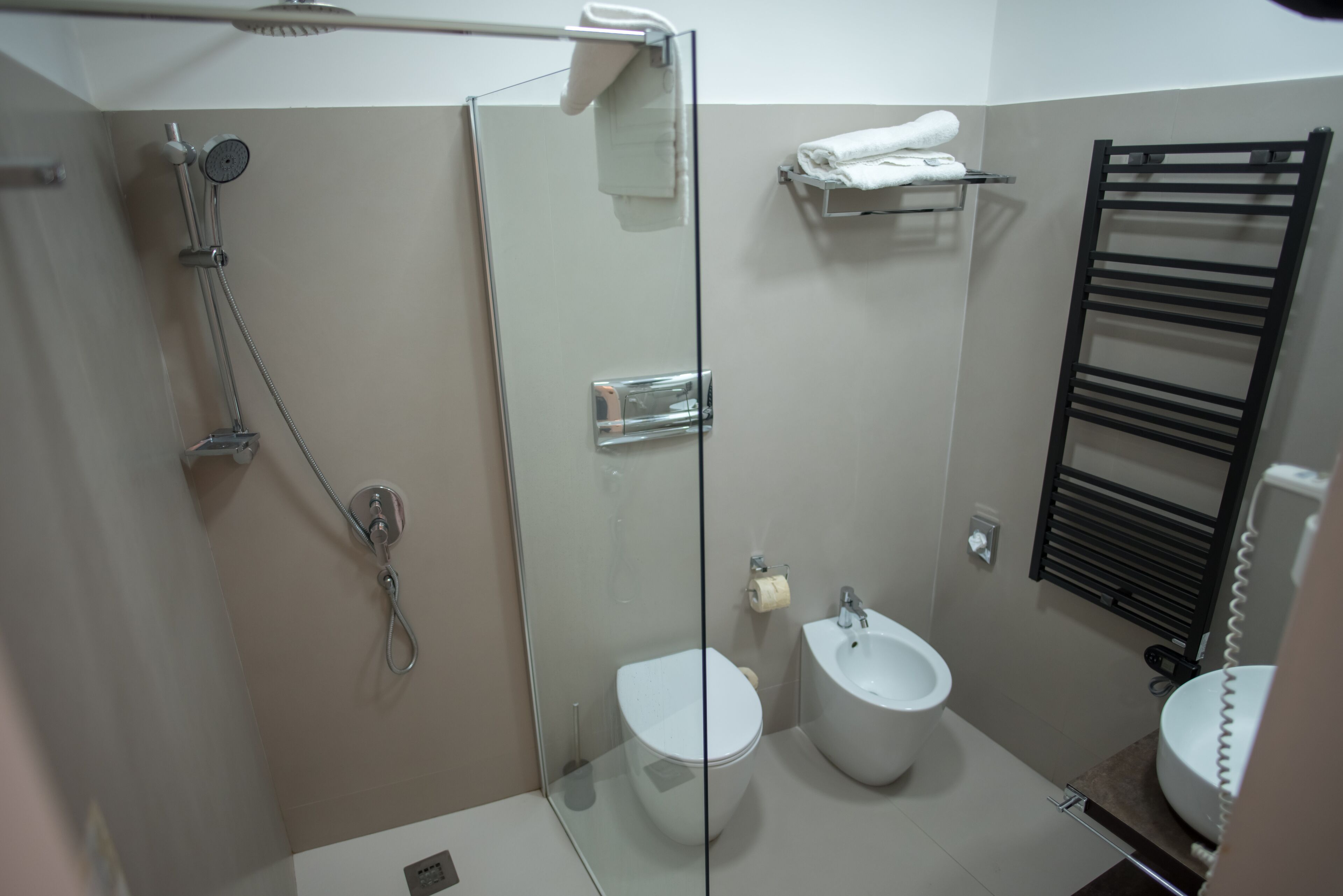 Un bagno moderno con box doccia in vetro, un bidet, un water e un portascopino.