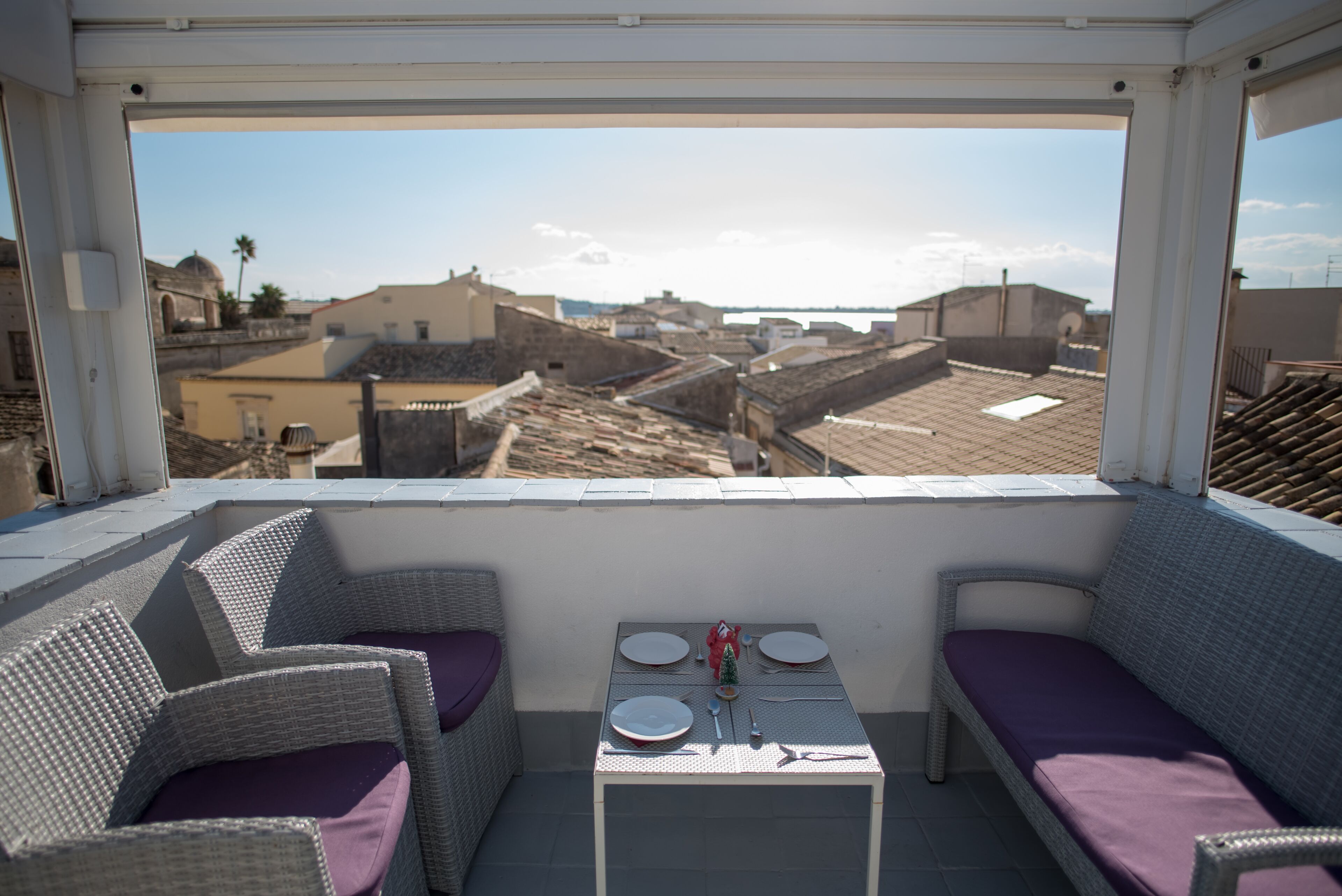 A balcony with wicker furniture, a table set for two, and a view of a cityscape.