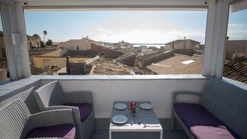 A balcony with wicker furniture, a table set for two, and a view of a cityscape.