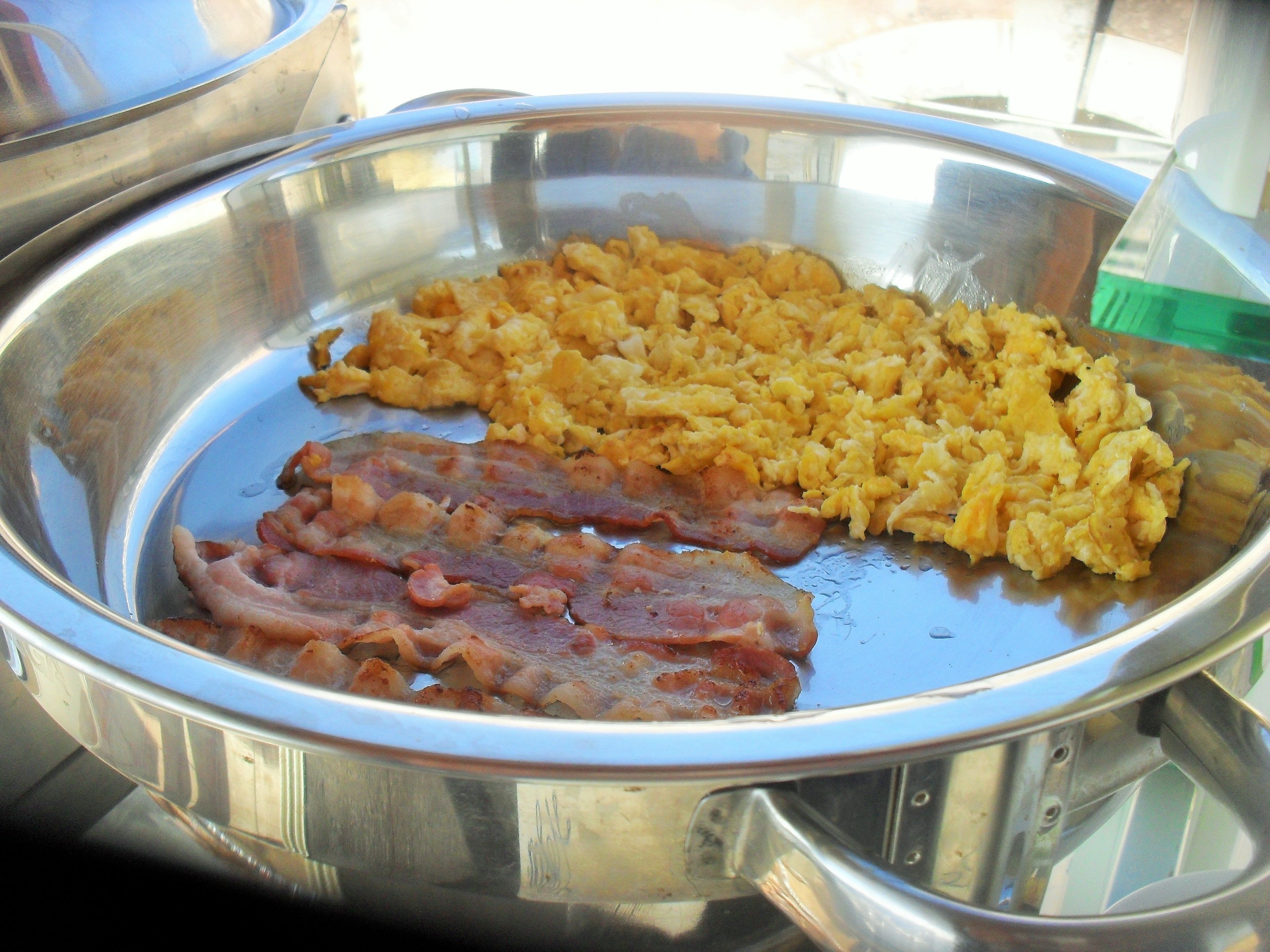 Uma travessa de aço inoxidável com ovos mexidos e bacon.
