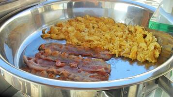 Uma travessa de aço inoxidável com ovos mexidos e bacon.