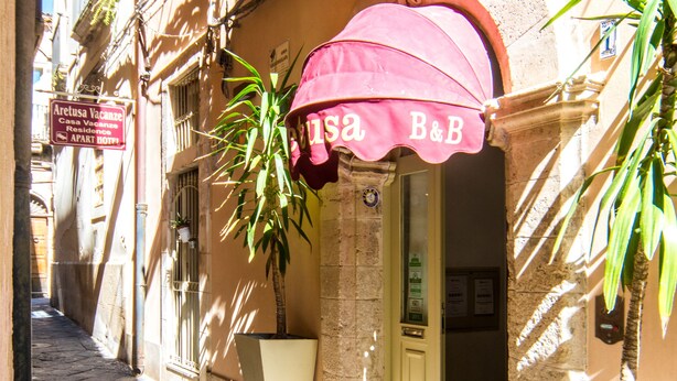 A narrow street with a building featuring a pink awning and a sign for 'Aretusa Vacanze'. - Aretusa Vacanze B&B (Syracuse)