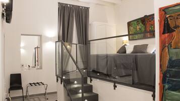 Un dormitorio moderno con una escalera de cristal, una cama con ropa de cama gris, un cuadro en la pared y una mesita de noche con una silla.