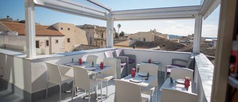 A rooftop terrace with tables and chairs, offering a view of the cityscape.