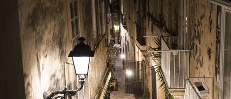 Un estrecho callejón flanqueado por edificios, con una farola y luces colgantes.