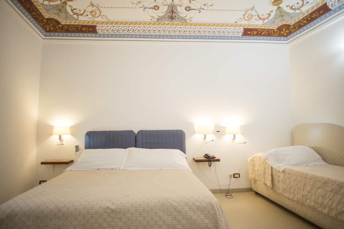 Habitación de hotel con una cama grande, dos mesitas de noche, dos lámparas de pared y una mesita auxiliar con un teléfono.